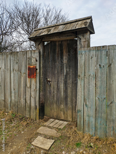 An old wooden gate with a canopy and a wooden fence in a village in Ukraine. A wooden garden door with an iron handle