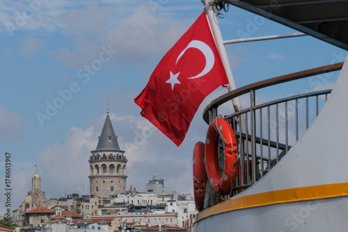A view of the Galata Tower in the historic old town of Istanbul, viewed across the water with the Turkish flag and boats shipping in the forground.