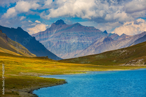 Small alpine lake, meadows and mountains under the beautiful sky in Aosta Valley, Italy.