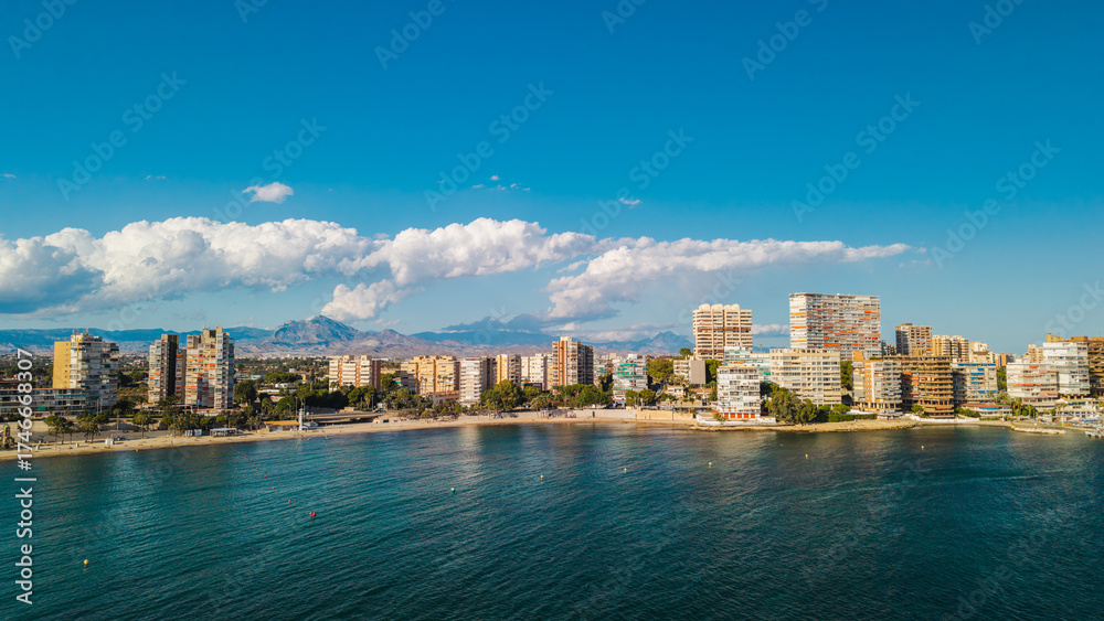 Fototapeta premium Aerial panoramic view of Alicante coastline in Spain with modern apartment buildings, sandy beaches, and turquoise Mediterranean water under a clear summer sky