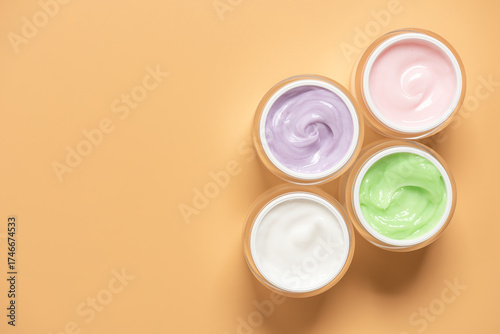 Set of colored cosmetic creams in open jars on pastel yellow background , top view, flat lay,