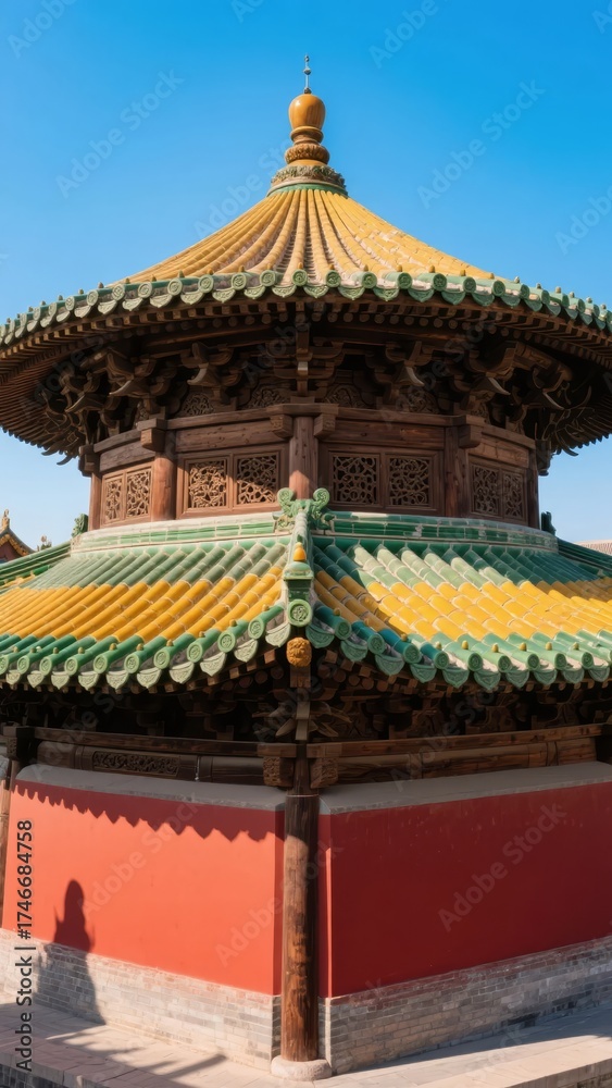 Fototapeta premium Traditional Chinese pavilion with ornate yellow and green tiled roof and red walls under a clear blue sky