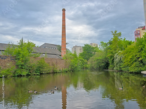 Old industrial building with chimney and green trees along Vilaine river in Rennes, france 