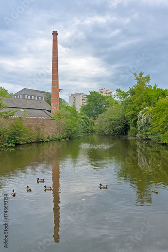 Old industrial building with chimney and green trees along Vilaine river in Rennes, france 