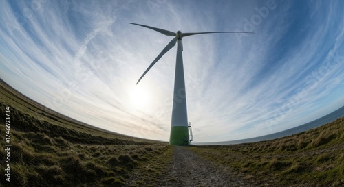 Wind turbine on grassy field under blue, cloud-streaked sky, panoramic view