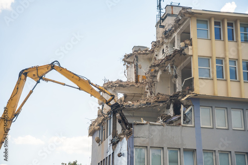 Powerful demolition of a concrete office building with a yellow high-reach excavator. Concept of transformation, destruction and construction renewal.
