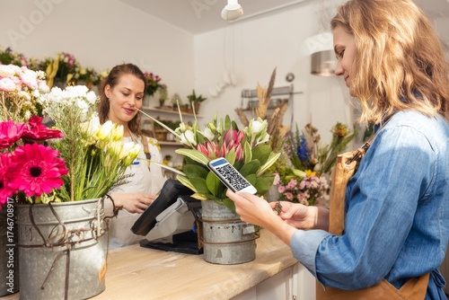 Young caucasian female customer scanning qr code in a vibrant flower shop.