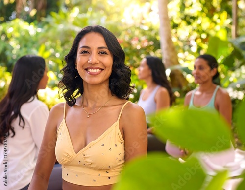 A woman smiles brightly, central to the frame, surrounded by greenery and three other women in the background. The scene is outdoors, bathed in sunlight