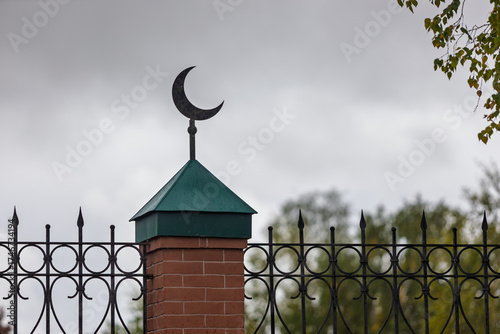 A close-up of a brick fence with metal crescent of Tatar mosque against an overcast sky at Yeniseysk in Krasnoyarsk krai, Russia.