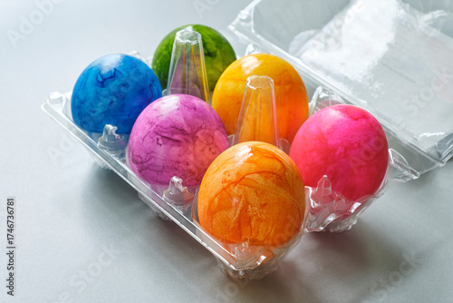 Plastic egg rack with colorful hand-painted Easter eggs in purple, blue, orange and yellow on a gray background. Image with copy space.	
