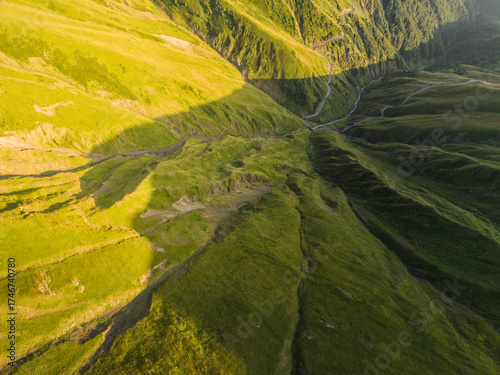 Aerial view of bright, sunlit green mountain slopes meeting in a shadowed valley, Alazani pass, Chala, Kakheti, Georgia.