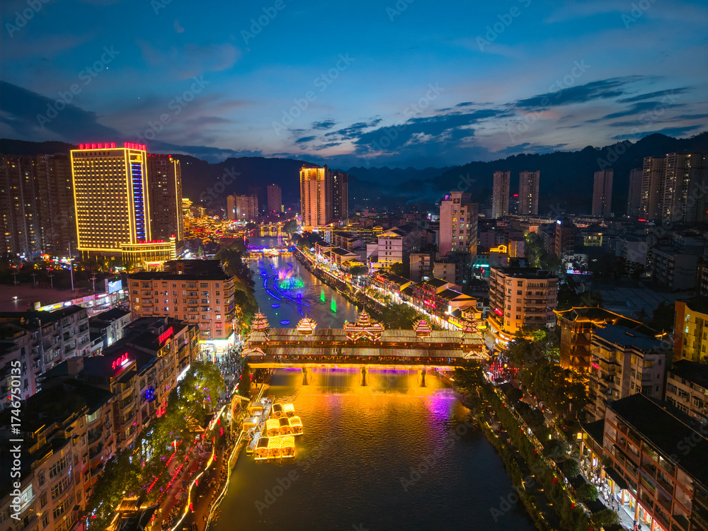 Obraz premium Xuan'en County Hubei Province China shines brightly with illuminated buildings along the river and bridge at twilight displaying vibrant colors