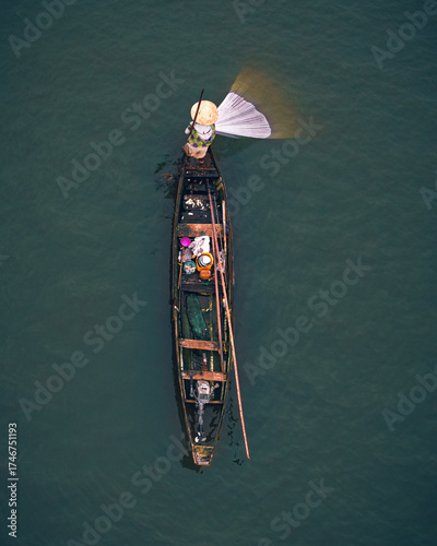 Aerial view of a solitary boat cuts through the still, dark waters, its occupant casting a net, creating a striking contrast of light and shadow, Epe, Lagos, Nigeria.