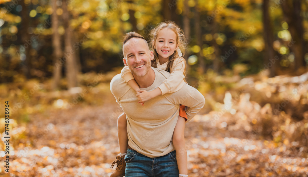Fototapeta premium Mature father giving piggyback ride to small daughter on a walk in autumn forest.