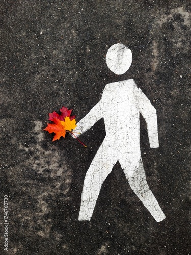 Pedestrian sign on the asphalt with a bouquet of autumn leaves in his hand. The concept of autumn walks, surprise, joy