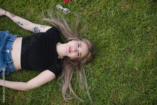 Young woman, beautiful, blonde, green eyes, relaxed and calm, seen from above, looking at the camera and lying on green grass. Concept of relaxation, peace, spring, grass.