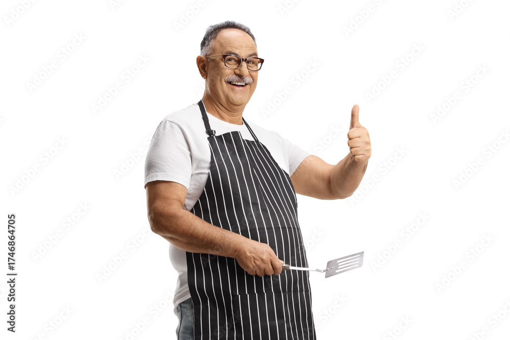 Fototapeta premium Mature man holding a turner utensil and gesturing thumbs up
