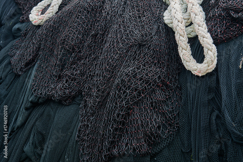 Close-up of dark fishing nets overlapped by a thick white braided rope, used in heavy maritime equipment. Rich texture ideal for backgrounds.
