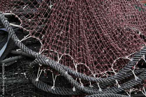 Detail of bundled fishing nets in black and burgundy tones, with thick coiled nautical ropes. Textural and color-rich marine composition.