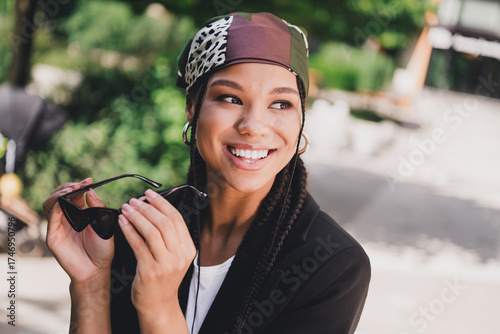 playful stylish woman smiles in sunny outdoor city park wearing headscarf and sunglass for travel fashion photo