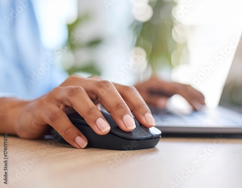 Woman's hand with a perfect manicure clicking a black wireless mouse on a wooden office desk.