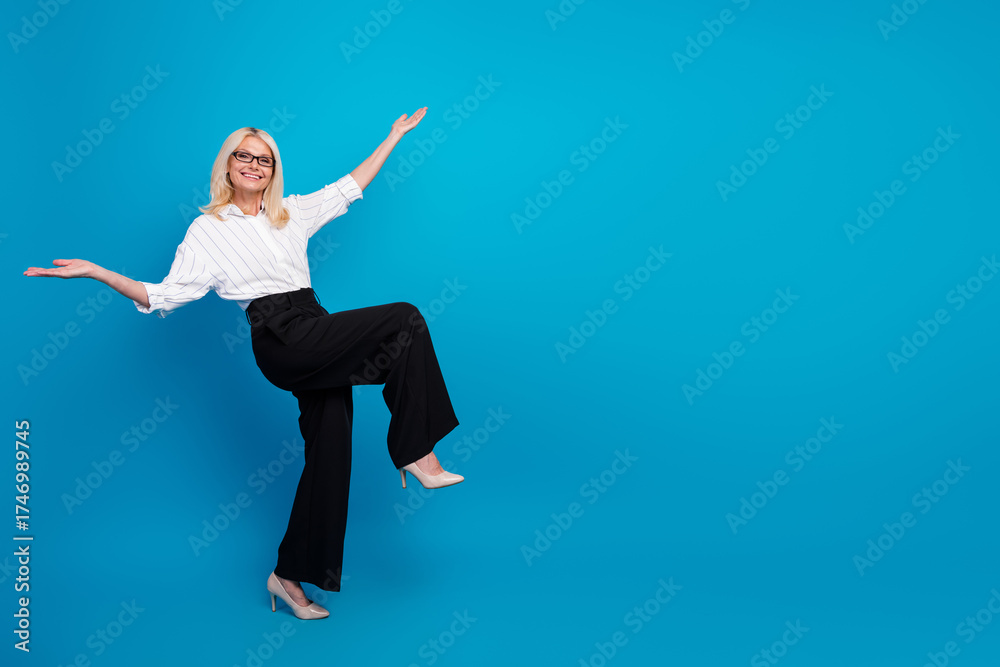 Obraz premium Confident mature businesswoman in blue studio with raised arms conveying professional energy and success