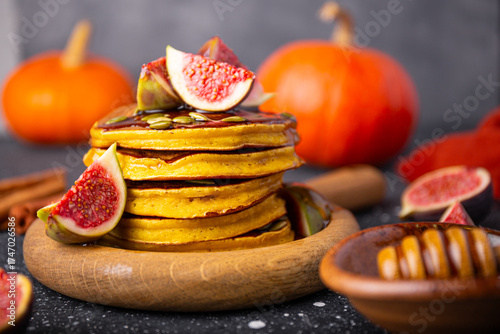 Stack of pumpkin pancakes with honey, pumpkin seeds and figs on a dark background. Concept of cozy homemade autumn food. Front view