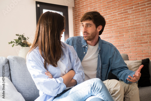Young couple sitting on sofa at home arguing and confronting each other, concept of relationship problems, breakup, jealousy, betrayal, lack of trust, or communication issues