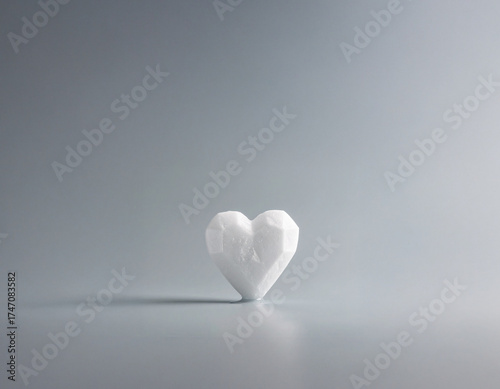 White geometric heart shape representing love, romance, passion, and emotional connection, casting a shadow on a serene gray background with copy space