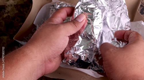 Hands unpacking delicious mexican food from a delivery box, unwrapping the foil to reveal tacos