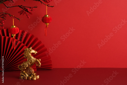 Golden horse figurine on coins with red lanterns and paper fans. Symbol of prosperity and strength in festive Chinese New Year 2026 setting.
