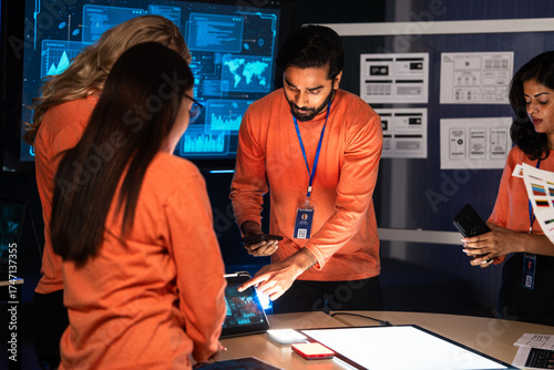 A diverse team of software engineers and UX,UI designers collaborates on a new mobile device. They are brainstorming a cybersecurity project, hardware, software or new technology launch