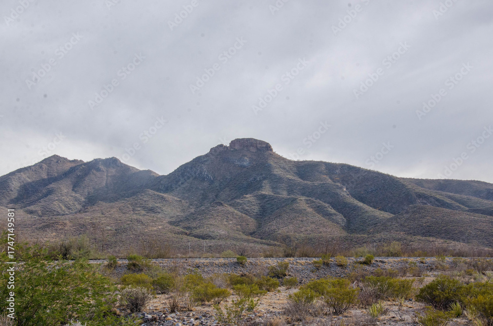 Obraz premium Explore rugged desert landscapes beneath a cloudy sky with mountains in the distance ideal for travel, adventure, and outdoor lifestyle projects