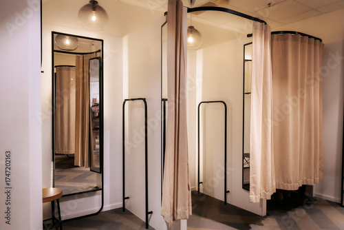 Quadro su tela Modern fitting room area in a clothing store with full-length mirrors, beige curtains, black frames, and soft ambient lighting creating a warm and private atmosphere