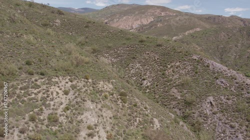 Drone flying over the mountains in southern Spain, the mountains have shrubs, there are some trees, and the sky has few clouds
