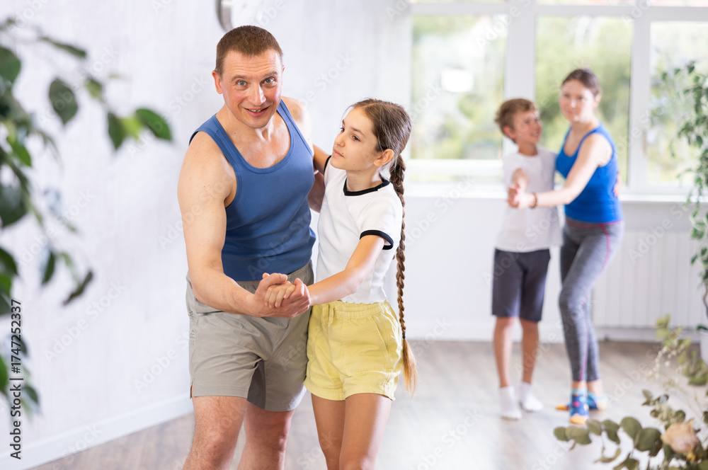 Fototapeta premium Active father and tween daughter training dance positions in pairs with family in light room
