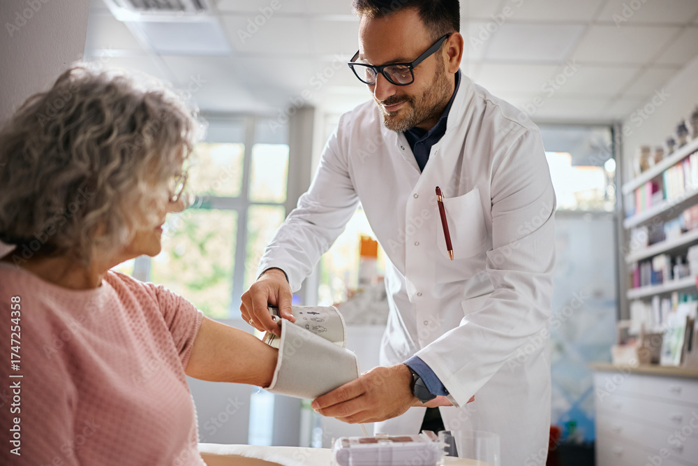 Obraz premium Happy doctor measuring blood pressure of senior woman in pharmacy.