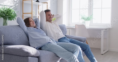Peaceful calm young couple relaxing on fashionable cozy sofa, resting at own house at relocation day, residential renovation, new room dreaming, enjoy together happy time alone, indoor comfy