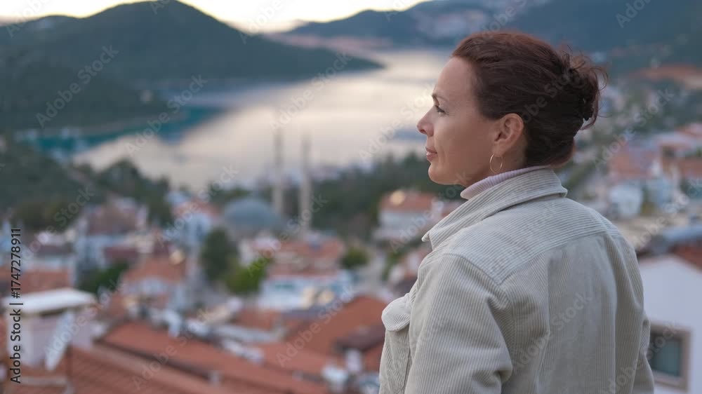 Woman admiring picturesque turkish coastal town. Scenic tourist experiencing panoramic vista of tranquil mediterranean bay. Overlooking traditional turkish architecture during golden hour in kas