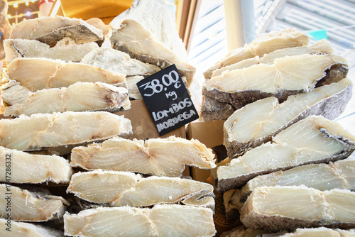 A large stack of premium, thick-cut, salted and dried codfish (Bacalhau) fillets on display with a handwritten price tag at the Mercado do Bolhão in Porto