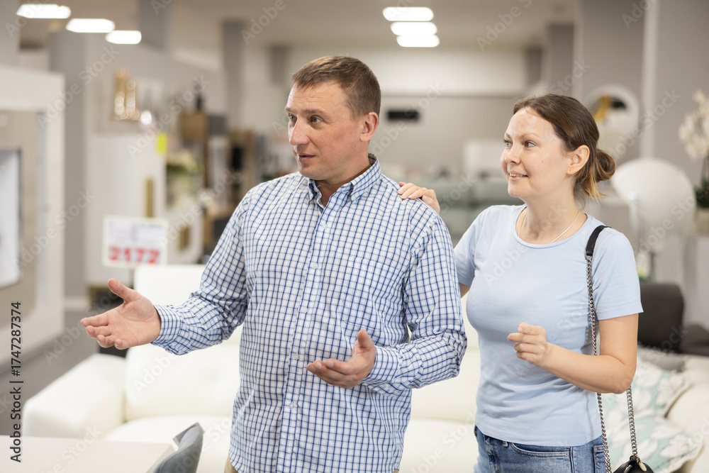 Fototapeta premium Interested man and woman strolling together through furniture showroom, curiously looking at various pieces for home and discussing choice