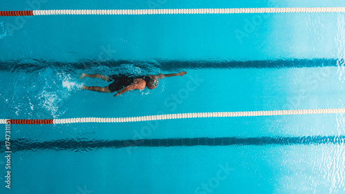 Принти на полотні Aerial top view of a swimmer in a blue pool performing freestyle stroke between lane dividers