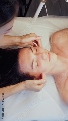 Woman professional massage therapist cosmetologist gives a facial massage against wrinkles to a beautiful client in a cosmetology room. Aesthetic cosmetology. Facial massage to prevent skin aging.