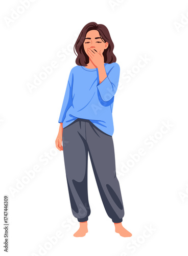 A sleepy young woman in blue pajamas yawning and covering her mouth, isolated on a white background.