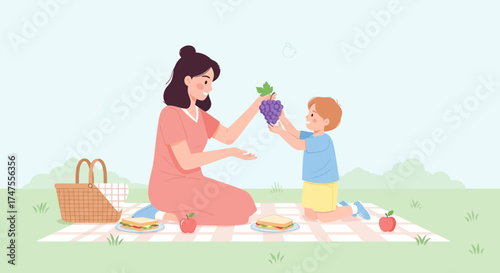 Mother and Son Sharing Grapes During a Picnic in a Park on a Bright Sunny Day