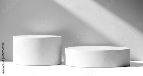 Two white marble cylindrical podiums of different heights placed on a white surface with soft shadow lighting on a plain textured gray background