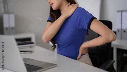 Asian woman office worker suffers shoulder back pain desk prolonged work focus workplace health ergonomics