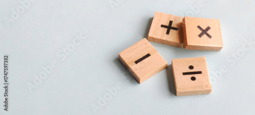 Fundamental arithmetic symbols on scattered wooden blocks against a soft blue background with clean copy space for educational and financial themes.