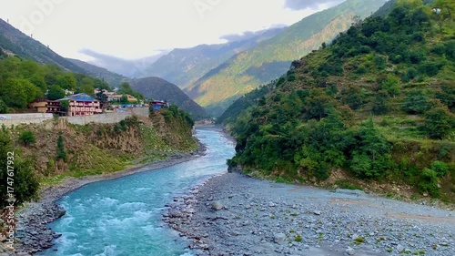 A dramatic panoramic landscape featuring the vibrant turquoise Swat River cutting through a lush mountain valley under a cloudy, atmospheric sky in Khyber Pakhtunkhwa, Pakistan.