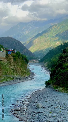 A dramatic panoramic landscape featuring the vibrant turquoise Swat River cutting through a lush mountain valley under a cloudy, atmospheric sky in Khyber Pakhtunkhwa, Pakistan.